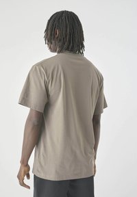 Brown, short-sleeve t-shirt made of cotton. The design features a rounded neckline and a relaxed fit, with stitching details visible.