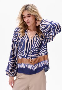 Fließende Bluse in Dunkelblau und Beige mit Zebra-Print, verfügt über einen V-Ausschnitt, lange Puffärmel und einen Kordelzug mit dekorativen Perlen.