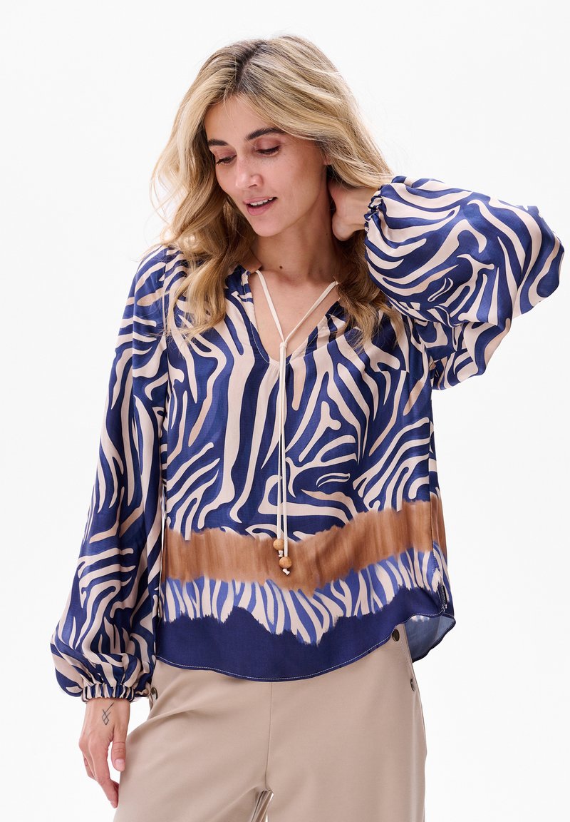 Fließende Bluse in Dunkelblau und Beige mit Zebra-Print, verfügt über einen V-Ausschnitt, lange Puffärmel und einen Kordelzug mit dekorativen Perlen.