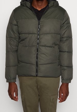 Homme portant une veste matelassée vert olive foncé avec capuche et fermeture éclair à l'avant, associée à un pantalon cargo assorti.