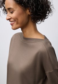 Brauner Strickpullover mit weitem Ausschnitt und gerippten Akzenten an den Schultern, weiche Textur und lockere Passform, von der Seite betrachtet.