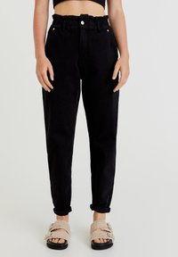 Svarta denimbyxor med samlad midja, raka ben och uppvikta fållar. Bärs med beigefärgade fluffiga sandaler med spänndetalj.