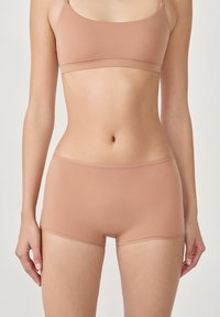 Bralette marrone chiaro e pantaloni boxer coordinati realizzati in un tessuto morbido e elasticizzato. Presenta un design semplice senza hardware o motivi visibili.