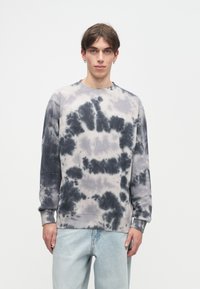 Sweatshirt em tie-dye cinza e preto, com mangas longas, decote redondo e punhos canelados. Logotipo discreto no peito. Corte solto.