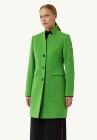 Grüner Wollmischungs-Mantel mit strukturiertem Kragen, einreihiger Knopfleiste mit schwarzen Knöpfen und Seitentaschen. Glatte Textur und taillierte Passform.