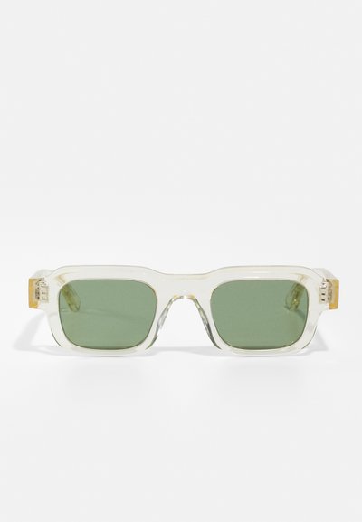 Gafas de sol con marco transparente y lentes verdes. Forma cuadrada, con un sutil acento dorado en las varillas. Textura suave, diseño moderno.