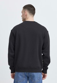 Schwarzer Baumwoll-Sweatshirt mit gerippten Bündchen und Saum, abgesenkten Schultern und rundem Rückenausschnitt, kombiniert mit hellblauen Jeans.