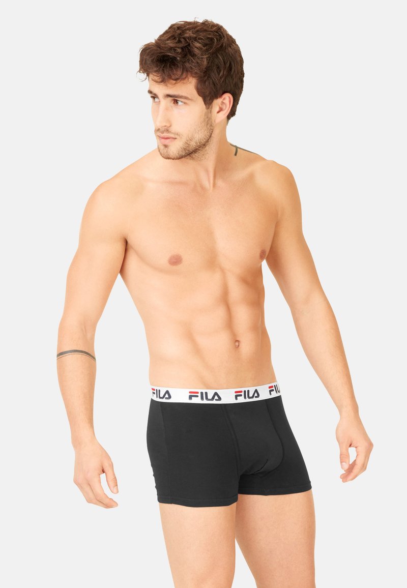 Boxer shorts noirs avec une ceinture blanche portant le logo Fila. Le tissu semble doux et le design est ajusté.