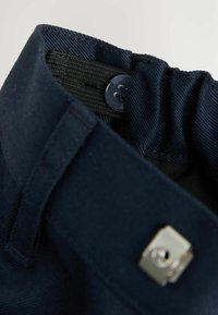 Marineblauem Stoffbund mit elastischem Einsatz, Knopfverschluss und silbernen Hardware-Akzenten. Glatte Textur mit strukturiertem Design.
