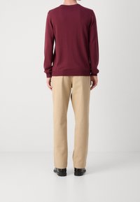 Burgunderfarbener, gestrickter Pullover mit langen Ärmeln, rundem Hals und gerippten Bündchen, kombiniert mit beigen, geraden Hosen und schwarzen Schuhen.