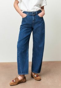 High-waisted, wijdbenige blauwe denim jeans met een riem, voorzien van voorzakken en een klassiek ontwerp met vijf zakken. Gestructureerde stof met subtiele vervaging.
