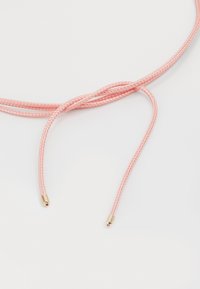 Vaaleanpunainen letitetty nauha, jossa on sileä pinta ja metallinhohtoiset kultaiset päät molemmissa päässä, esitetty kevyttä taustaa vasten.