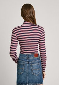 Top de manga larga a rayas en azul marino, rojo y blanco, combinado con una falda de mezclilla que cuenta con dos bolsillos traseros y una etiqueta de cuero en la cintura.