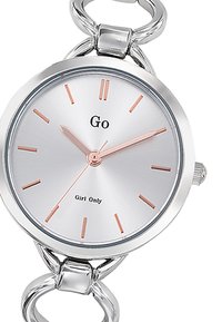 Montre argentée avec un cadran rond, accents en or rose, design de bracelet à maillons, et texte noir indiquant "Go Girl Only". Marqueurs d'heure minimalistes.