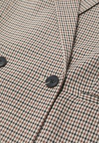Brown and cream houndstooth patterned fabric with black accents, featuring two black buttons and a notched lapel detail.