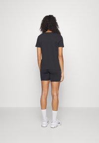 Camiseta negra de manga corta combinada con pantalones cortos negros. La modelo lleva calcetines blancos hasta el tobillo y zapatillas deportivas gris claro. Silueta limpia y minimalista.