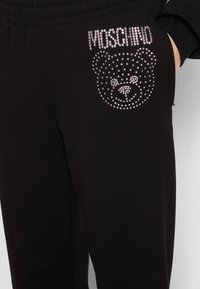 Schwarze Jogginghose mit weicher Textur, mit einem Strassbär-Design und dem auf der Seite platzierten "Moschino"-Logo verziert.