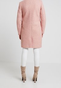 Abrigo texturizado rosa con mangas largas, corte recto y detalles de costura. Combinado con leggins blancos y botas de tacón beige.