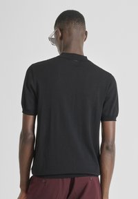 Crna kratka majica s ovratnikom, izrađena od lagane tkanine, s blagom teksturom i ravnim rubom.