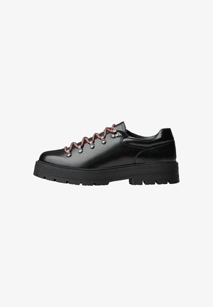 Chaussure de randonnée en cuir noir avec des lacets rouges et blancs, de grands œillets et une semelle épaisse à crampons pour une bonne adhérence et stabilité.