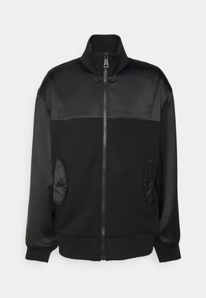 Melna jaka ar matētu un satīna virsmu kombināciju, augstu apkakli, rāvējslēdzēju un sānu kabatām ar pogu akcentiem. Gluda tekstūra.