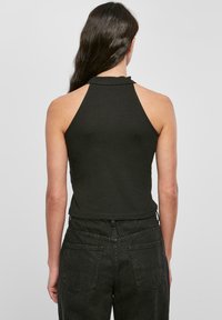 Svart ärmlös haltertop med hög halsringning, figursydd design och slät textur, kombinerad med högmidjade mörka jeans med bakfickor.