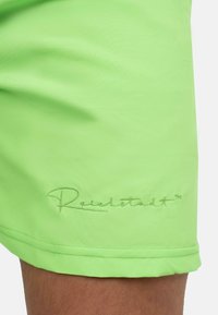 Limoengroene zwembroek van soepel, lichtgewicht stof, met een gestikte Reichtstadt-logo in een lichtere groentint op de zoom.