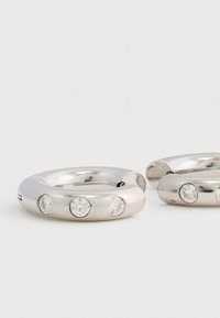 Ασημένια στρογγυλά σκουλαρίκια με τρία διαφανή κοσμήματα ενσωματωμένα σε μια λεία, στρογγυλή σχεδίαση. Αντανακλαστική επιφάνεια και αόρατος μηχανισμός κλεισίματος.