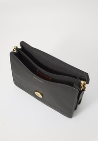 Sac à main en cuir noir avec une texture lisse, doté d'un fermoir rond en or, de deux compartiments et d'un subtil détail de couture le long du bord.