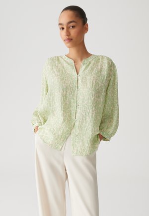 Light green, patterned shirt with a loose fit, long sleeves, and a button-up front, paired with cream trousers. Textured, lightweight fabric.