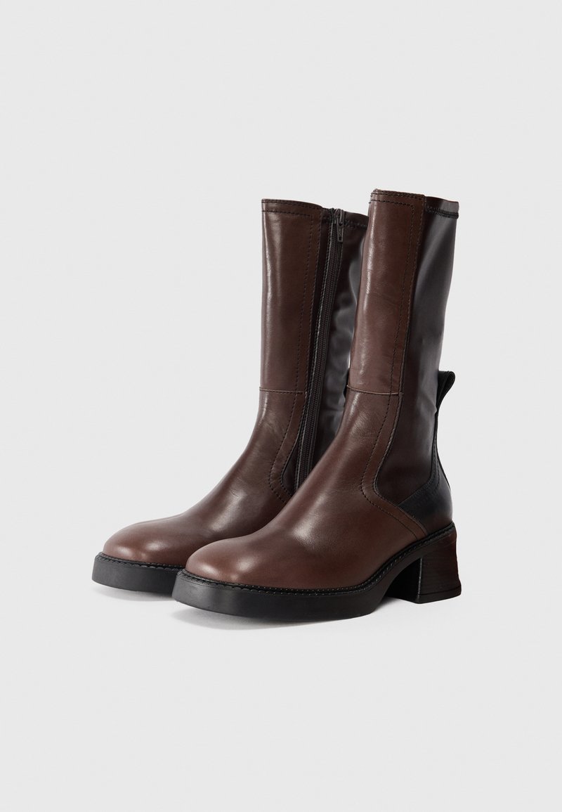 Bottines en cuir marron avec un bout arrondi, fermeture éclair sur le côté et un talon empilé. Présente des accents en cuir noir contrastants.