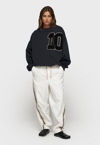 Felpa oversize blu scuro con un grande design bianco e nero "10", abbinata a pantaloni bianchi larghi con strisce laterali.
