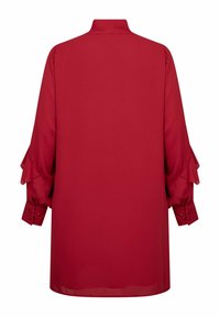 Ilgi piedurkņu sarkans blūze ar augstu apkakli, pogājamiem manšetēm un slāņainiem frills detaļām uz piedurknēm, parādīta no aizmugures.