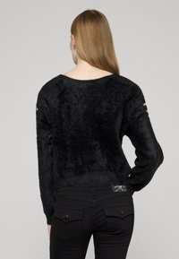 Czarny, miękki sweter z okrągłym dekoltem i długimi rękawami, zestawiony z czarnymi jeansami z tylnymi kieszeniami i ozdobnym przeszyciem.