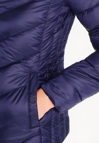 Tmavě modrá péřová bunda s horizontálním prošívaným vzorem, přední kapsou a hladkou, lesklou texturou.