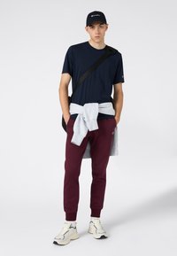 Camiseta azul marino, pantalones de chándal color burdeos, suéter gris atado a la cintura, bolso cruzado negro y zapatillas beige con detalles en negro.