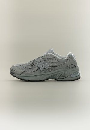 Sneaker sportiva New Balance grigia con pannelli in mesh e scamosciato, chiusura con lacci, suola imbottita, mostrata di profilo su sfondo neutro.