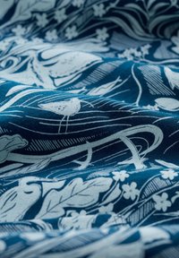 Tela azul con intrincados patrones de naturaleza en blanco que presentan pájaros, hojas, flores y líneas fluidas.