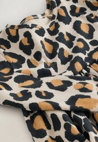 Begge leopardprint langærmet topp i beige med sorte og brune pletter, lavet af ribbet stof. Har en rund halsudskæring og sammensnørende detaljer.