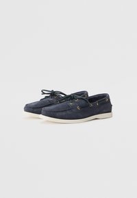 Marineblå suede båt sko med avrundet tå, hvit gummisåle, gulløyeler og mørkegrønne lisser. Enkelt design med minimalt med detaljer.