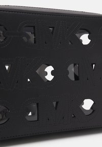 Borsa in pelle nera con motivo a intaglio del logo MK, texture liscia e sezioni trasparenti a contrasto. Dettagli cuciti lungo i bordi.