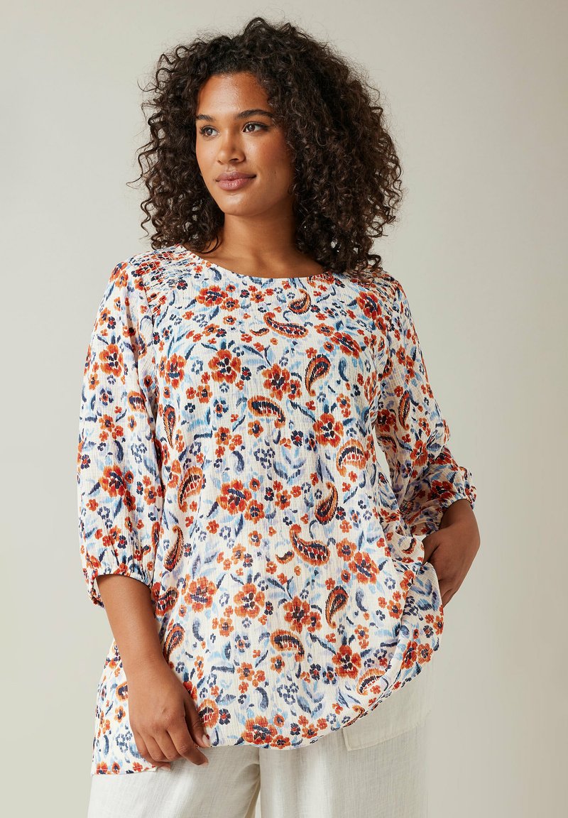 Bluse i let materiale med blomsterprint, rund halsudskæring, 3/4 ærmer og en afslappet pasform. Farverne inkluderer blå, orange og hvid.
