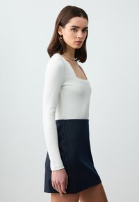 Top bianco a maniche lunghe con coste e scollatura quadrata abbinato a una mini gonna blu navy a righe. Texture liscia, colori contrastanti.