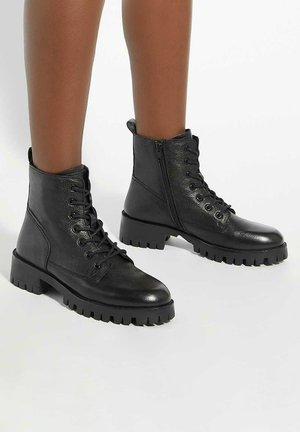 Black leather ankle boots with a textured finish, featuring a lace-up front, side zipper, and chunky rubber soles with tread detailing.