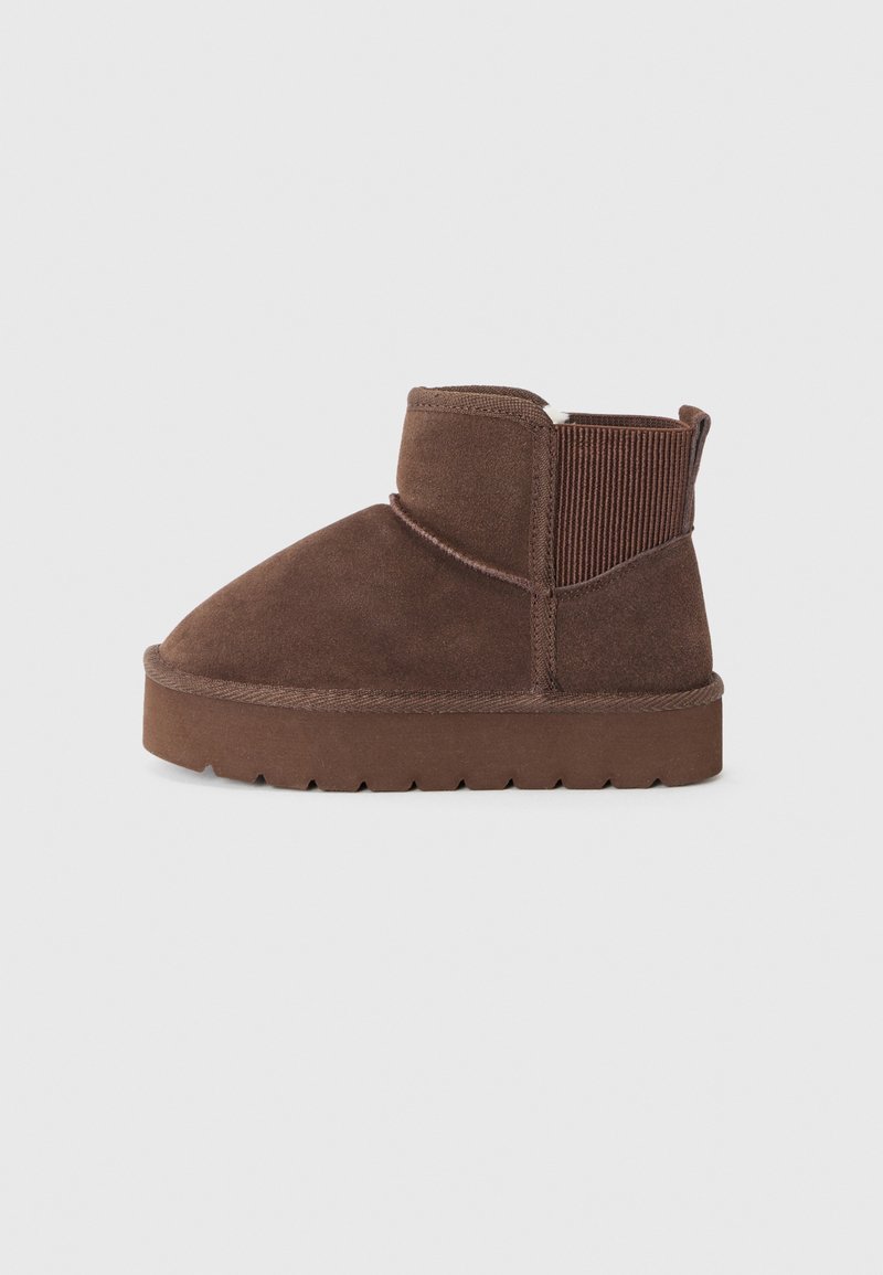 Botas de tornozelo em camurça castanha com painéis laterais elásticos, bico redondo e sola de borracha texturizada. Apresenta um design sem emendas e um estilo minimalista.
