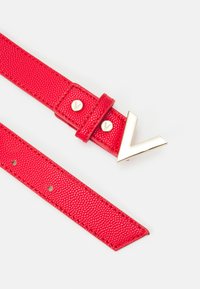 Ceinture rouge texturée avec une boucle en métal doré en forme de V et deux clous décoratifs. Comprend des trous ajustables pour la variation des tailles.