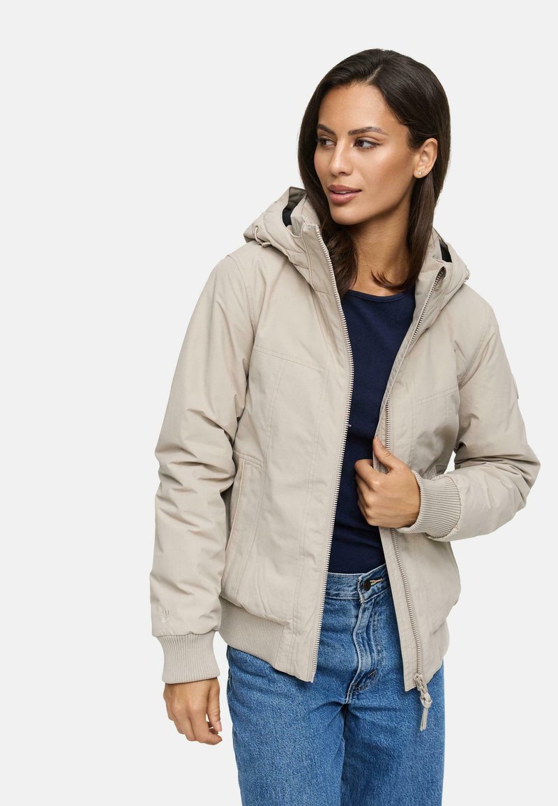 Beige hoodie met een rits aan de voorkant, geribbelde manchetten en twee zijzakken. Draagt over een marineblauwe top en gecombineerd met blauwe jeans.