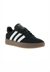 Sneaker in suede nero con strisce bianche e suola in gomma marrone. Presenta punta rotonda, superficie testurizzata e logo dorato sulla linguetta.