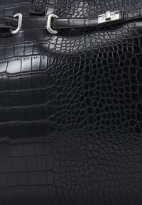 Svart krokodilpräglad läderväska med en glänsande yta, silverfärgad hårdvara och en strukturerad design med accentremmar.