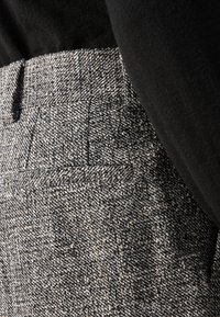 Pantaloni grigi strutturati con un sottile motivo a spina di pesce, dotati di tasche laterali e vestibilità sagomata, abbinati a un top nero.